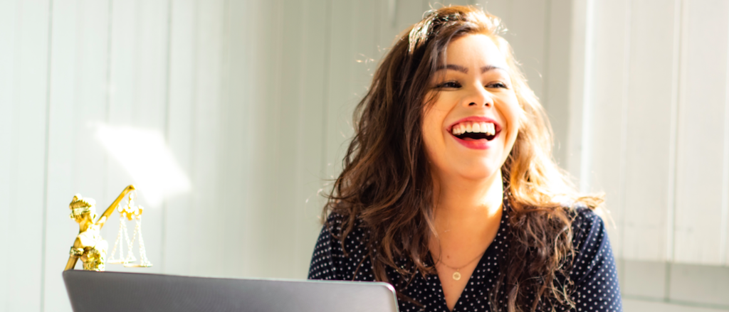 Student laughing in front of their laptop and a statue of lady justice.